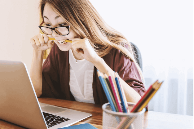 Stressed out Asian girl biting a pencil while looking at her laptop