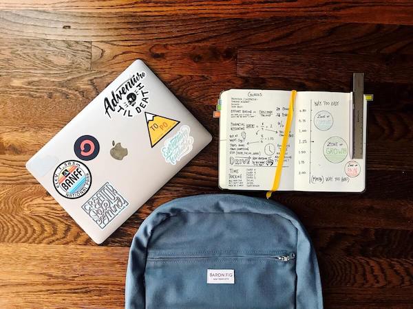 Laptop, diary and bag placed on a wooden floor.