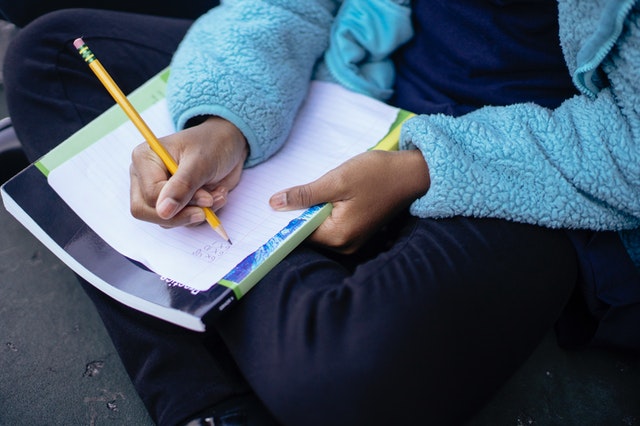 Student sitting cross-legged and doing rough work on a piece of paper supporting it on a register.